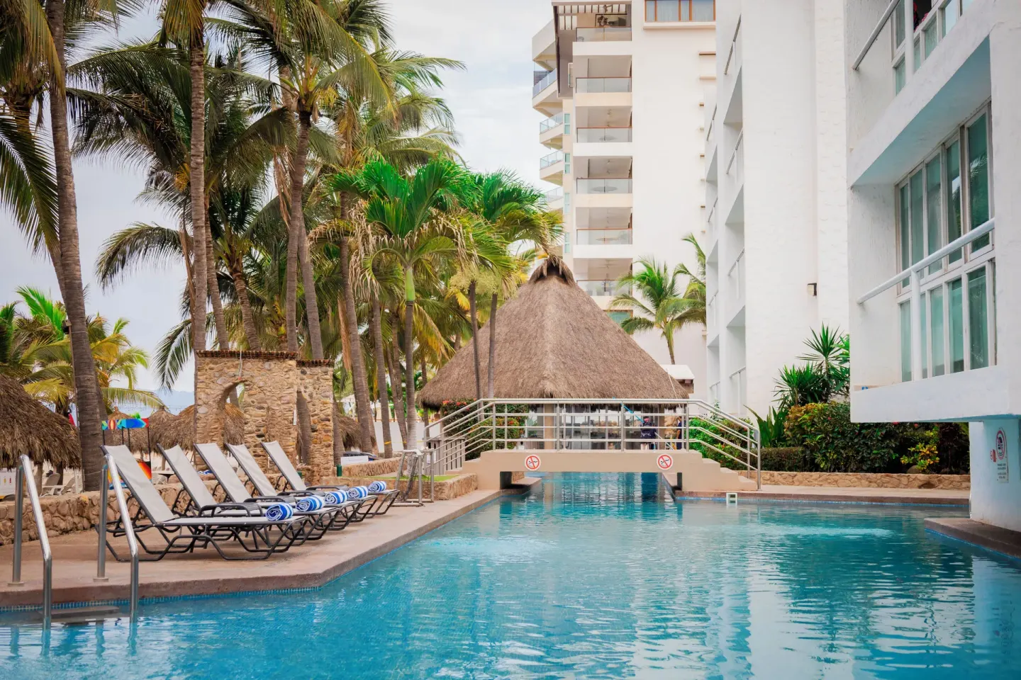 Pool with lounge chairs, palms, and a thatched structure at Villa Varadero.