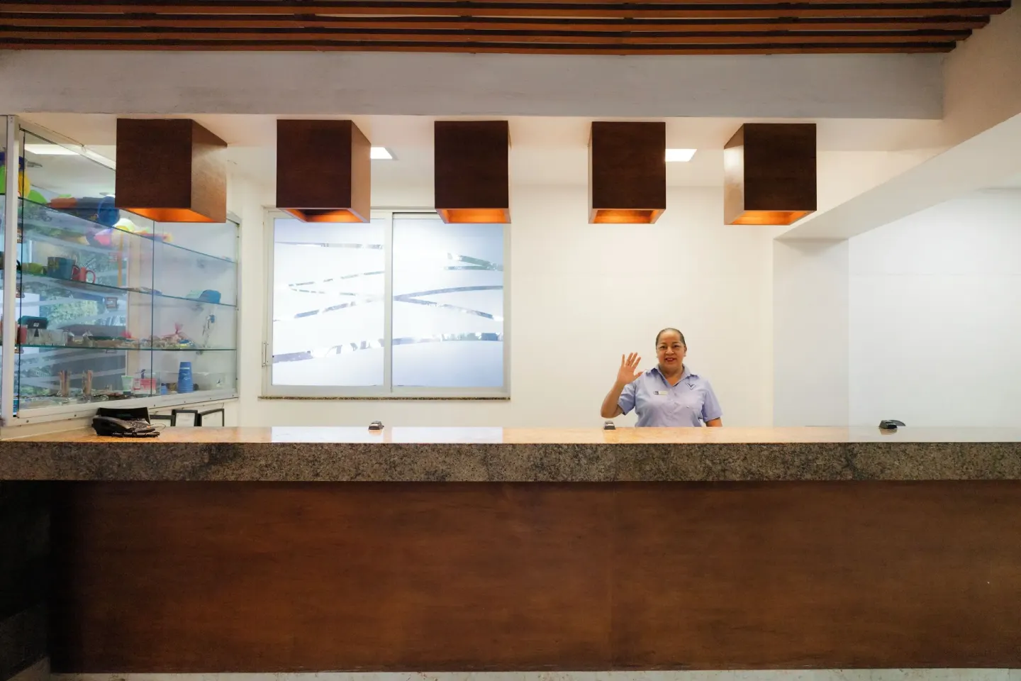 Reception counter with a staff member waving beneath square lights at Villa Varadero.
