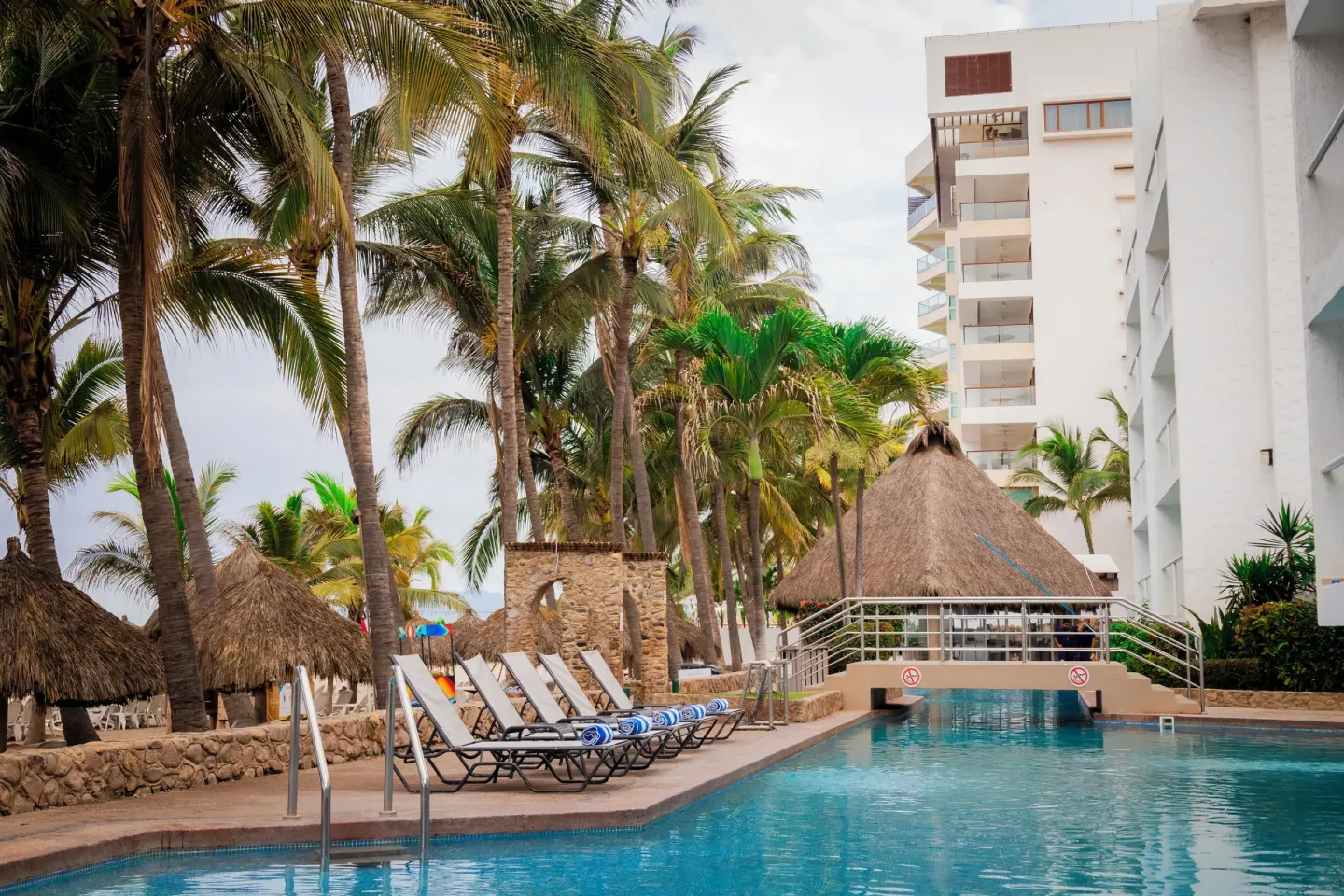 Pool deck with palm trees, loungers, and thatched shade at Villa Varadero.