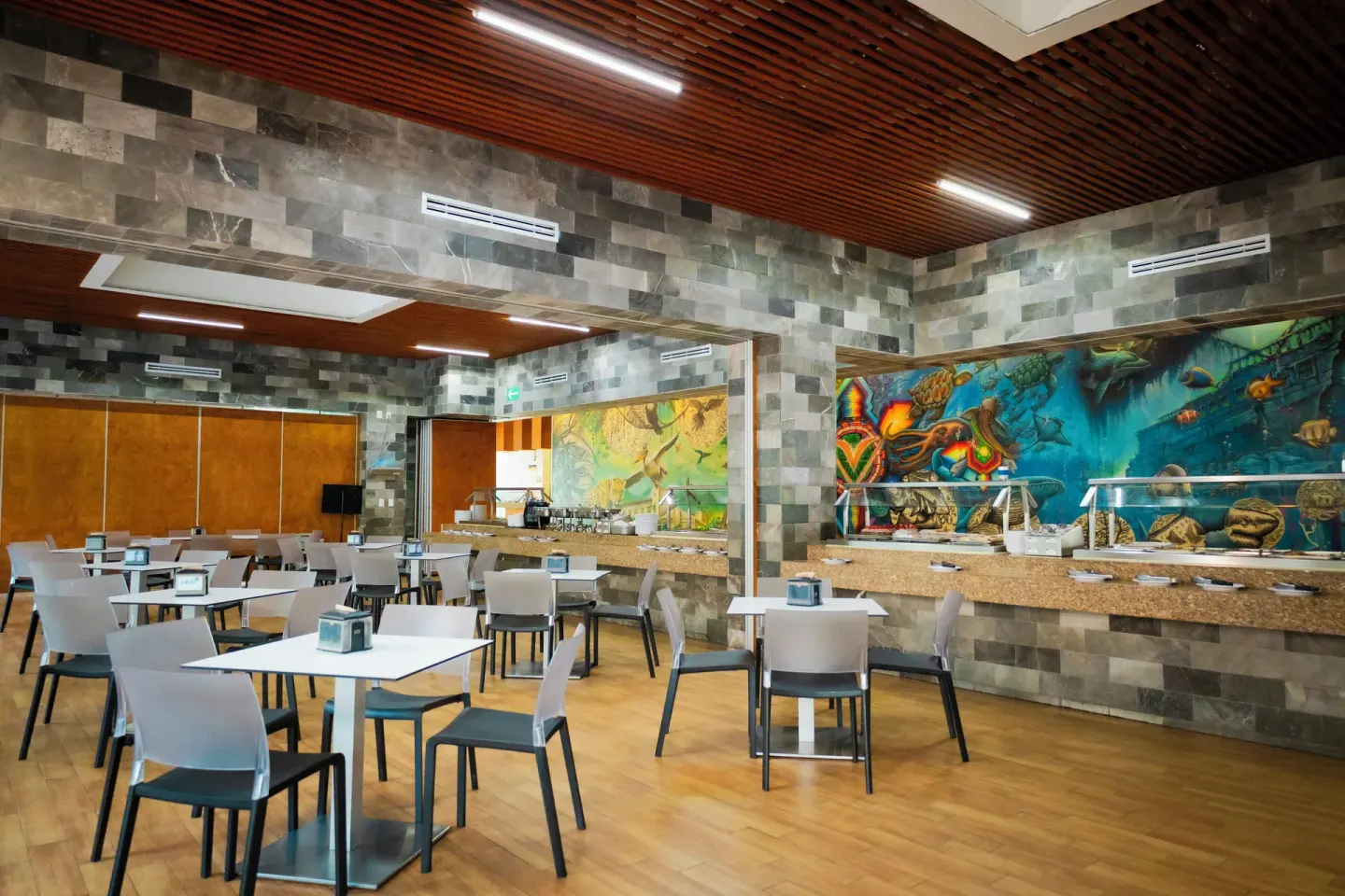 Buffet dining room at Villa Varadero with white tables, stone walls, and colorful murals.