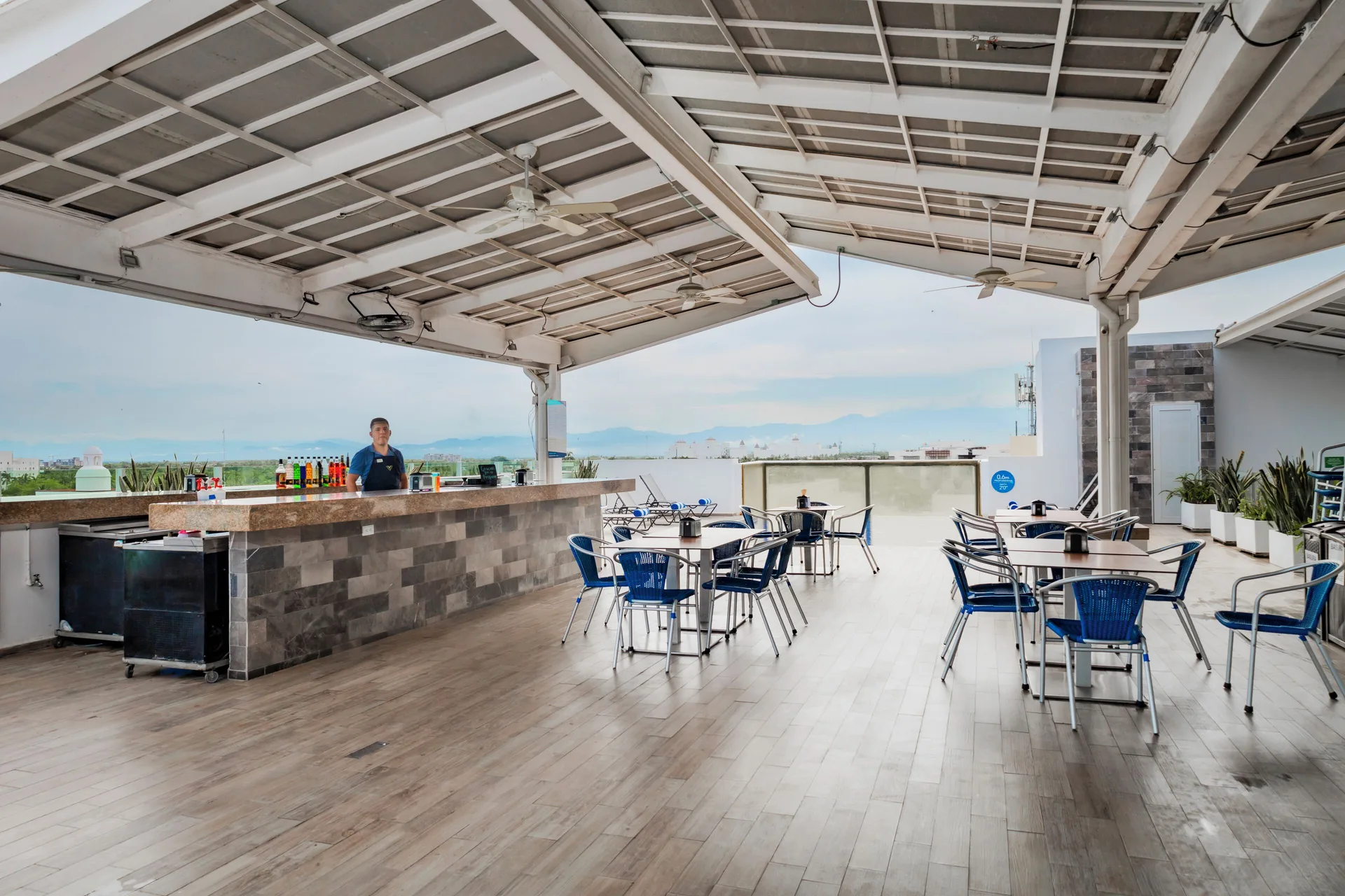 Open-air rooftop bar terrace with tables and blue chairs at Villa Varadero.
