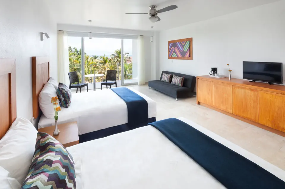 Deluxe Room with two beds, sofa, TV, and palm-view balcony at Villa Varadero.