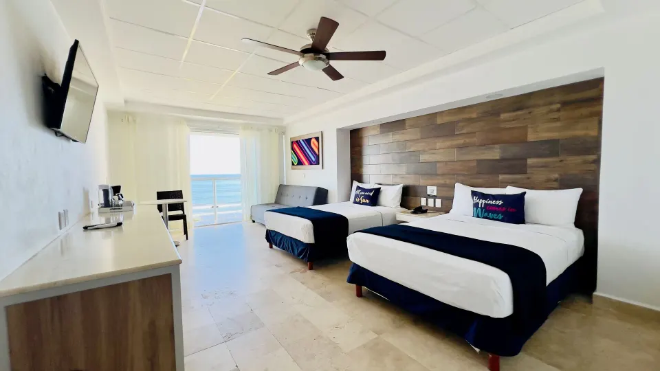 Junior room at Villa Varadero with two beds, desk, TV, ceiling fan, sofa, and balcony sea view.