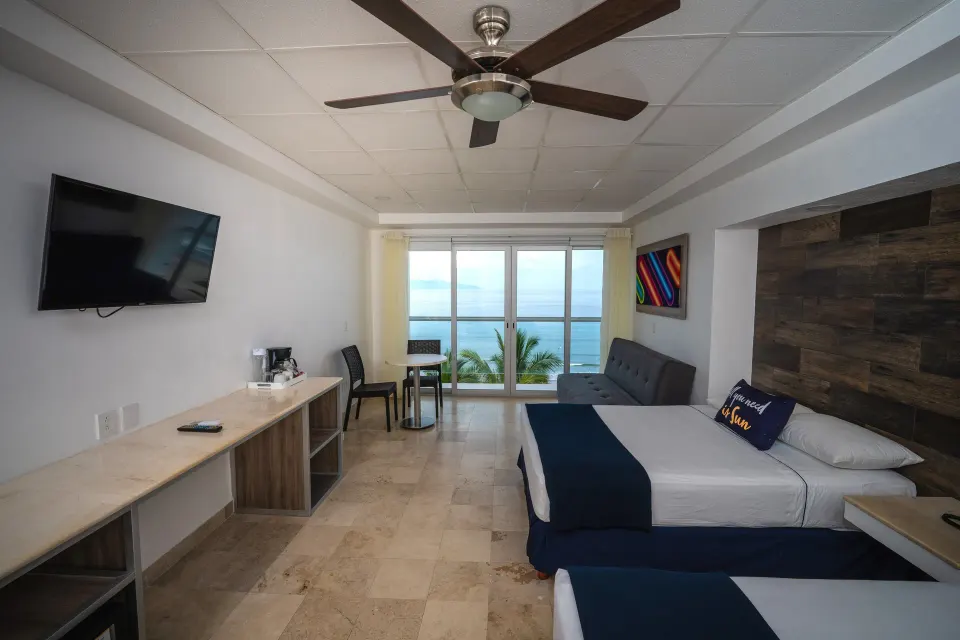Junior room at Villa Varadero with two beds, sofa, ceiling fan, desk, TV, and sea-facing balcony doors.