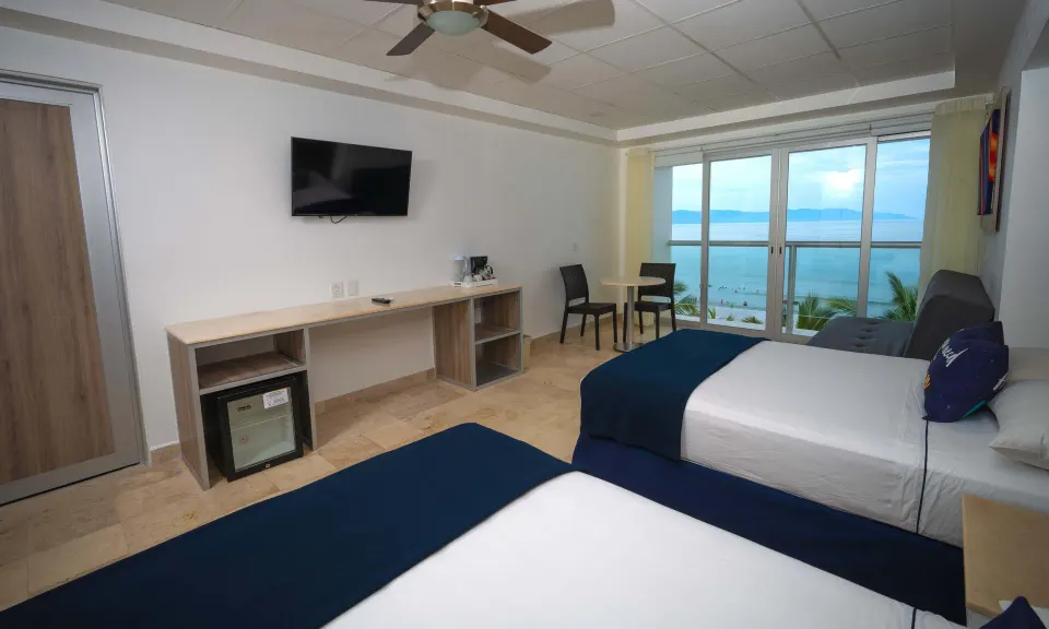 Junior room at Villa Varadero with two beds, wall TV, desk, mini fridge, and balcony sea view.
