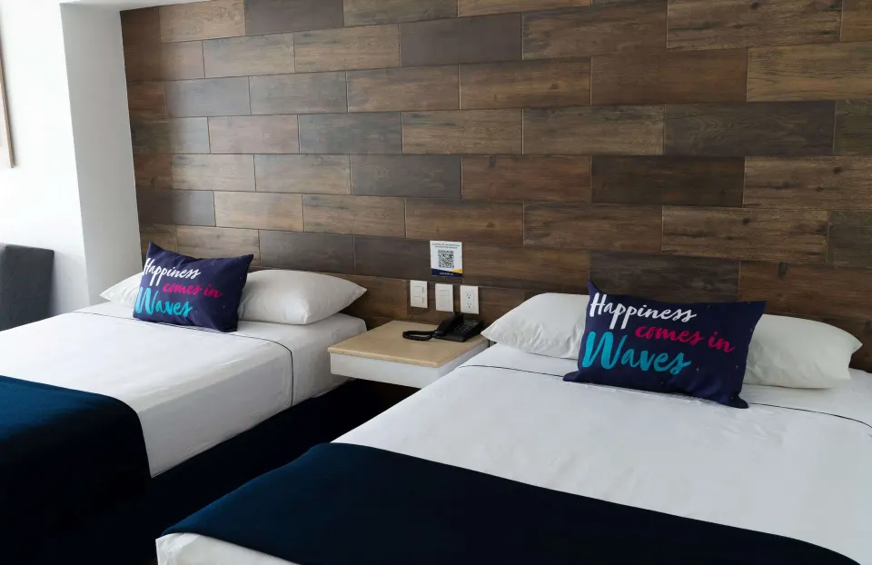 Junior room at Villa Varadero with two beds, white linens, accent pillows, and a wood-look headboard wall.