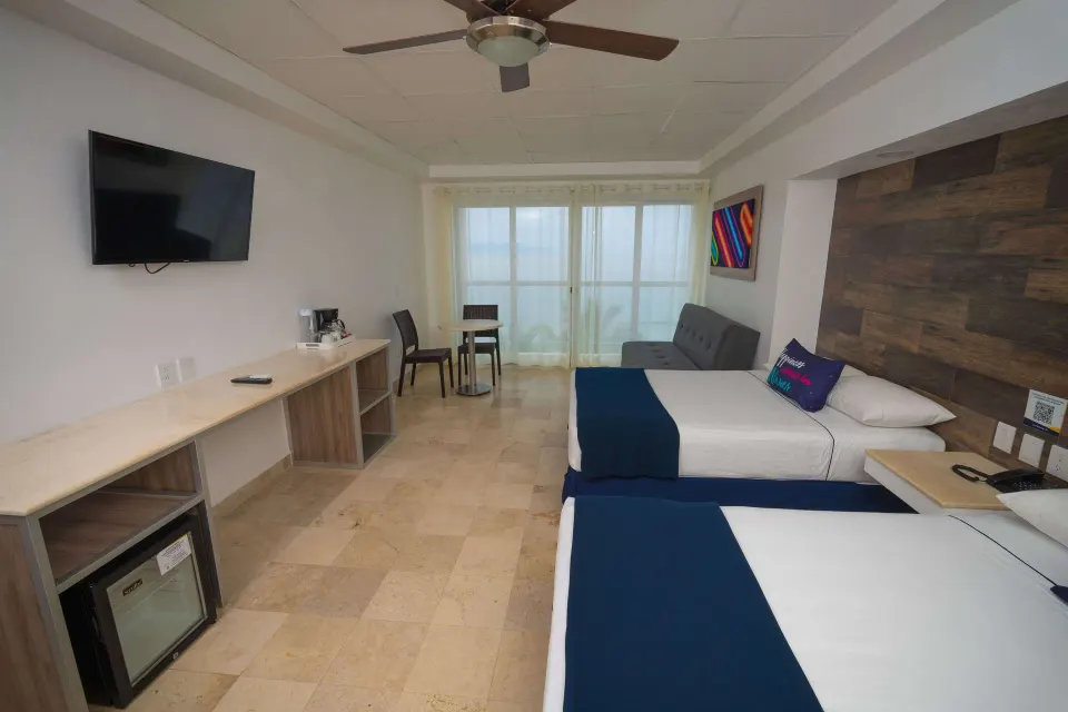 Junior room at Villa Varadero with two beds, desk, TV, mini fridge, coffee setup, and sheer balcony curtains.