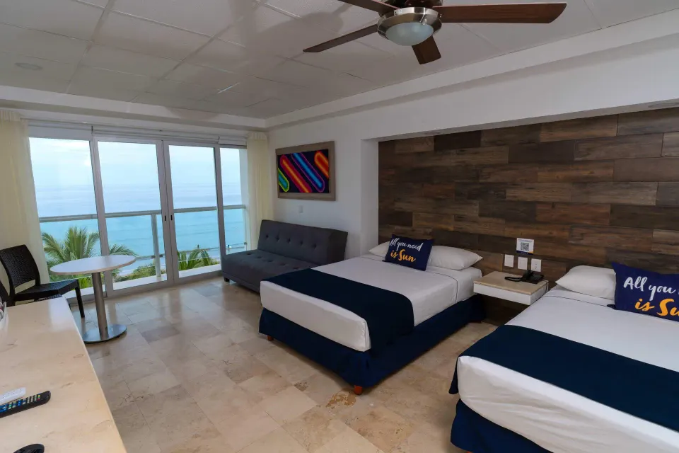 Junior room at Villa Varadero with two beds, sofa, table, balcony doors, and ocean view.