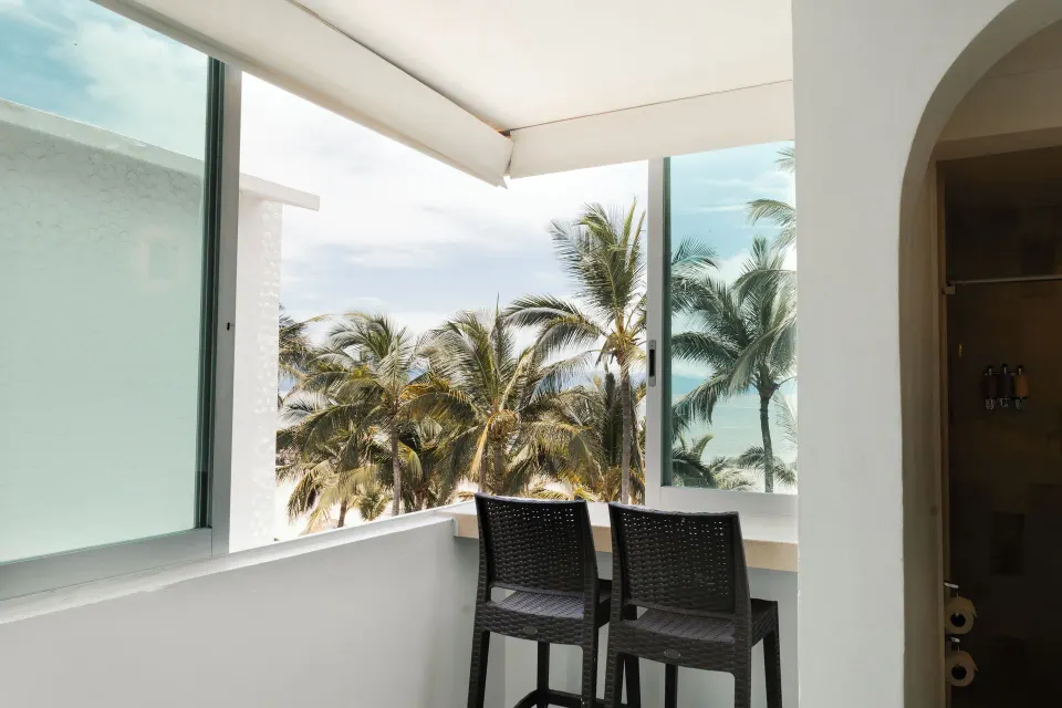 Standard Room balcony at Villa Varadero with two chairs, palm trees, and ocean beyond the windows.