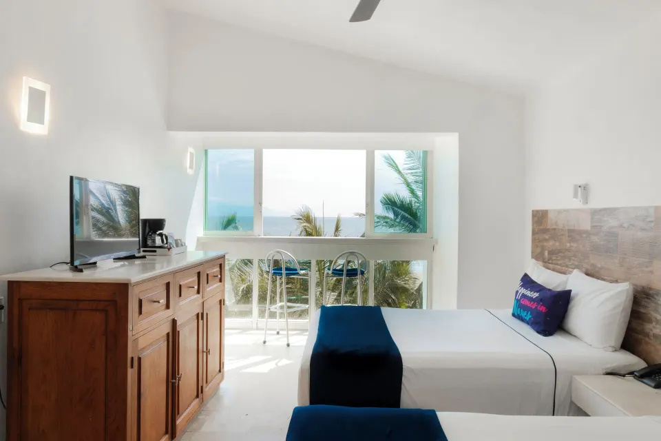 Standard Room at Villa Varadero with two beds, TV dresser, coffee maker, and ocean view from the window.