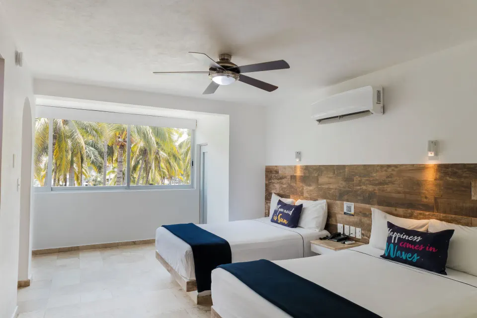 Standard Room at Villa Varadero with two beds and a wide window looking onto palm trees.
