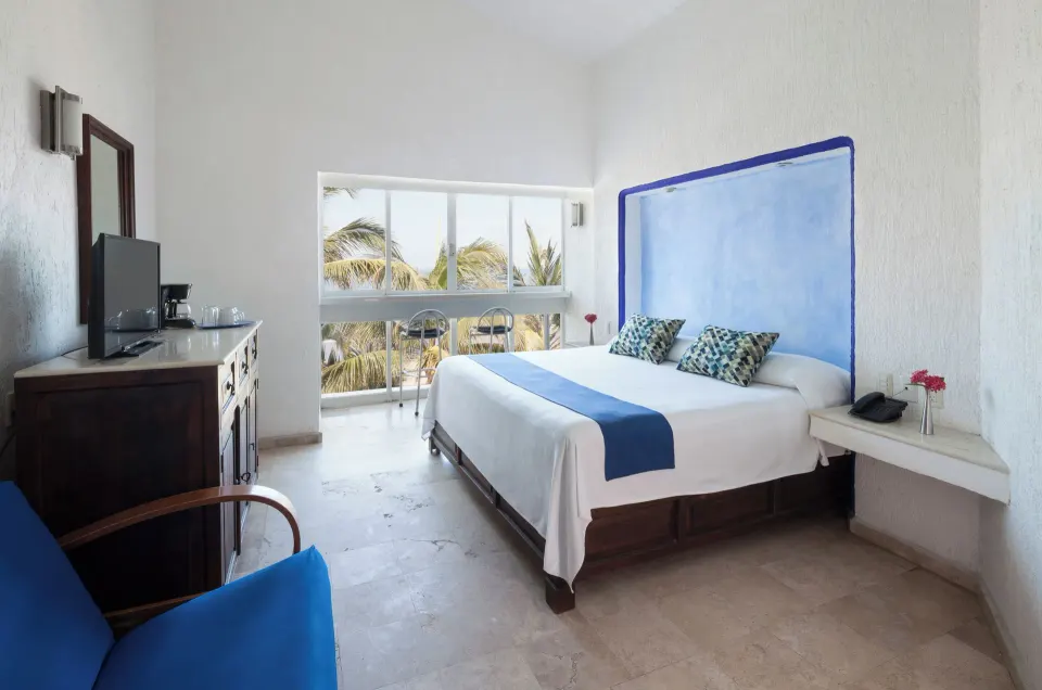 Superior Sea View room with king bed, blue headboard, TV cabinet, and palm view at Villa Varadero.