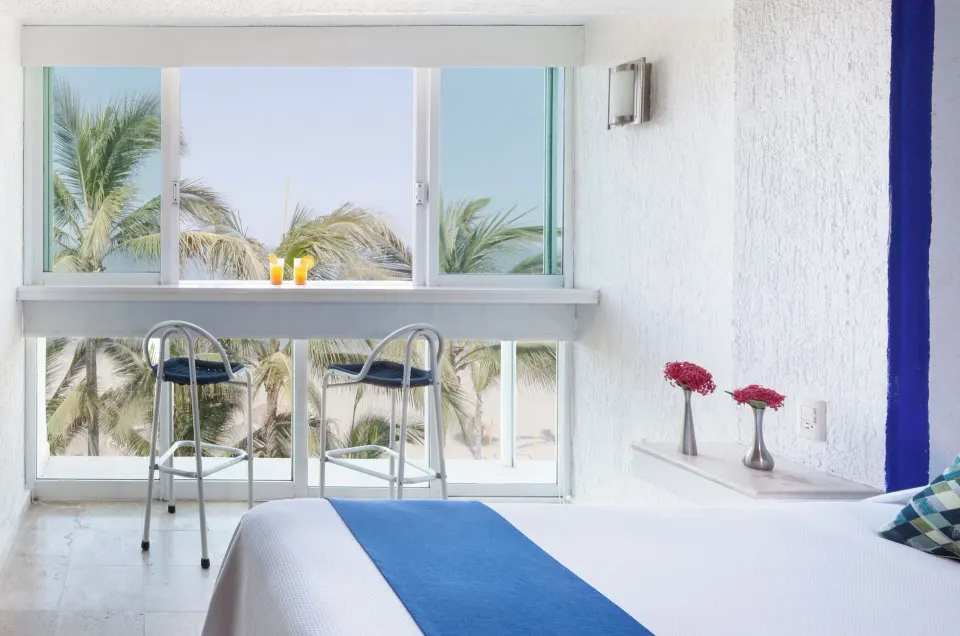 Superior Sea View room window with bed corner, stools, palms, and beach at Villa Varadero.