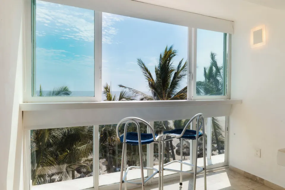 Superior Sea View room window with two stools, palms, and ocean beyond at Villa Varadero.