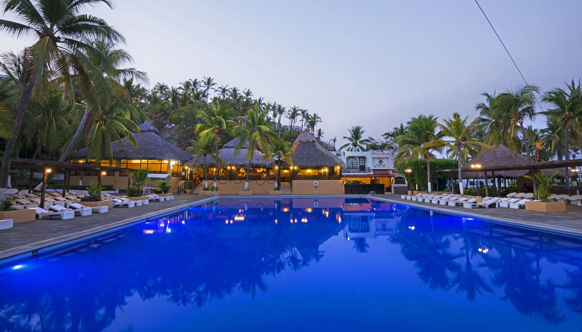 Evening view of the main pool with palapas at Vista Playa de Oro Manzanillo.