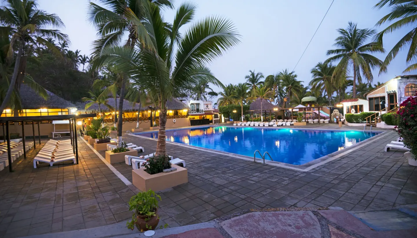 Large evening pool area with palms and lounge chairs at Vista Playa de Oro Manzanillo.