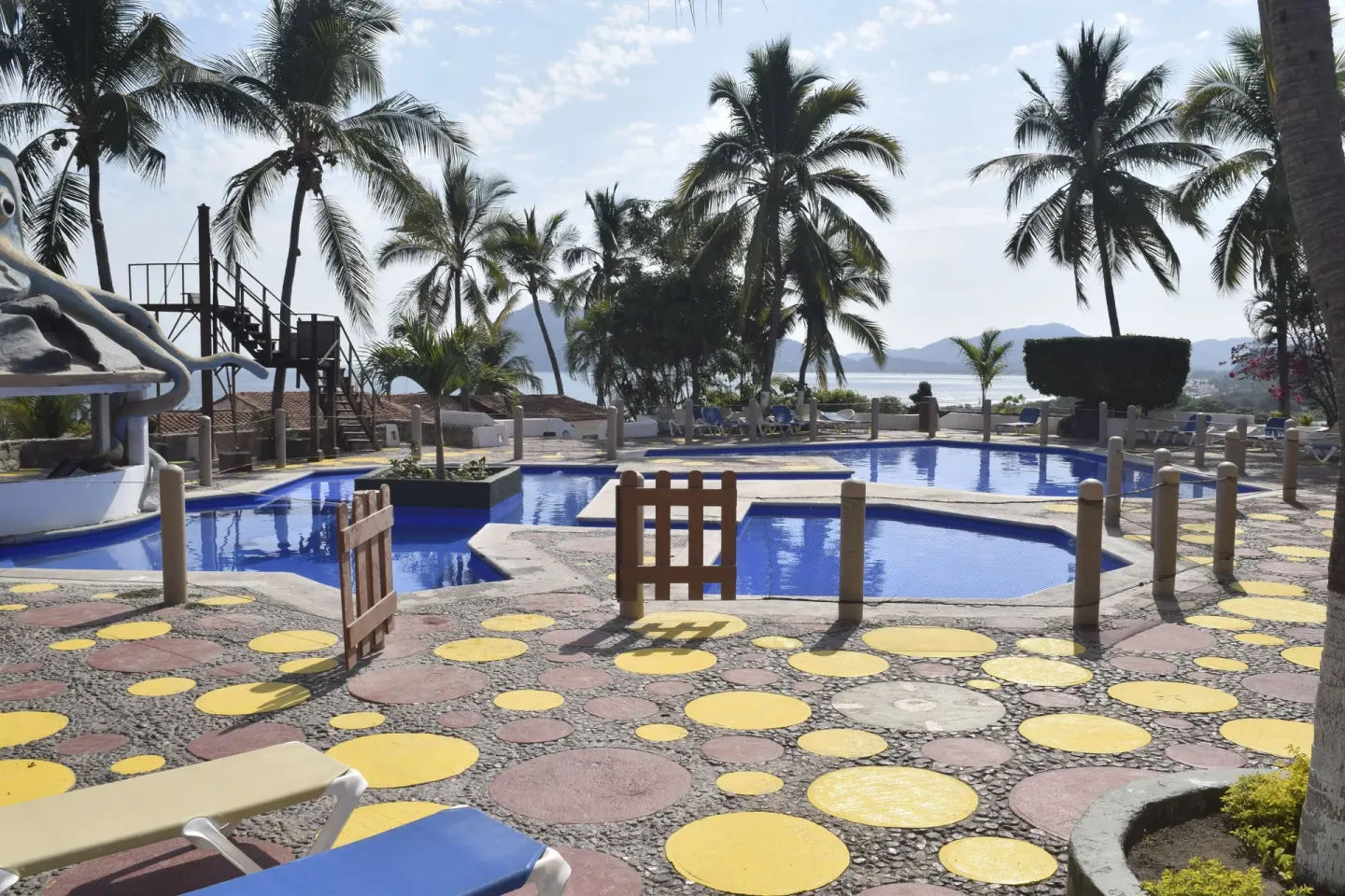 Pool area with palms, lounge chairs, and ocean in the distance at Vista Playa de Oro Manzanillo.