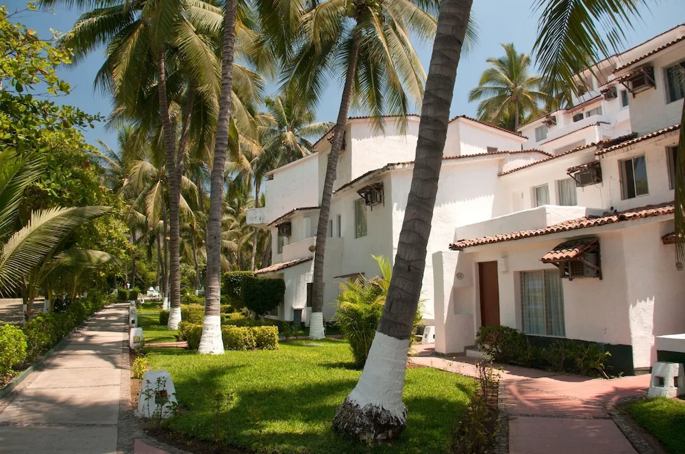 Palm-lined walkway beside white guest buildings at Vista Playa de Oro Manzanillo.