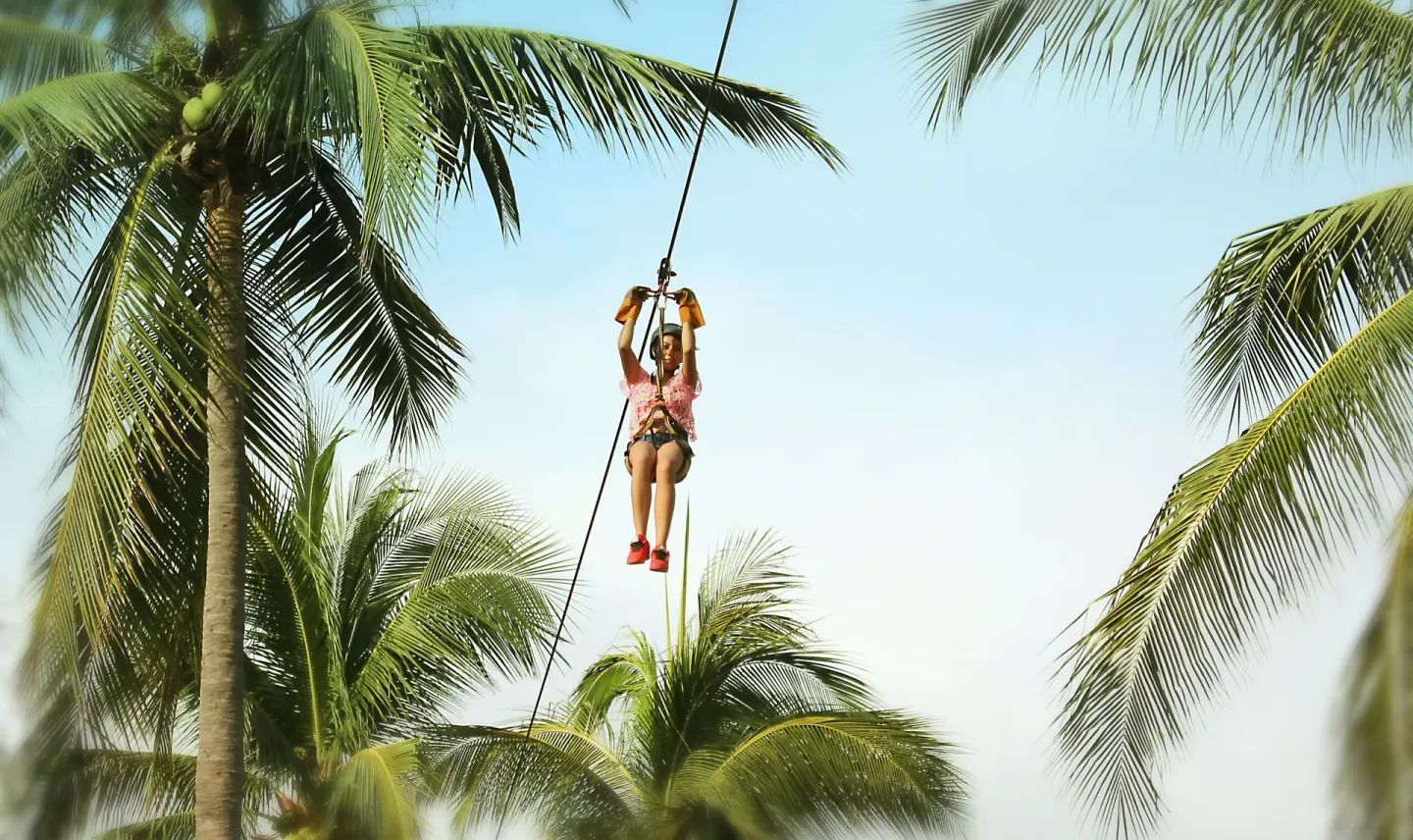 Child riding a zip line through palm trees at Vista Playa de Oro Manzanillo.