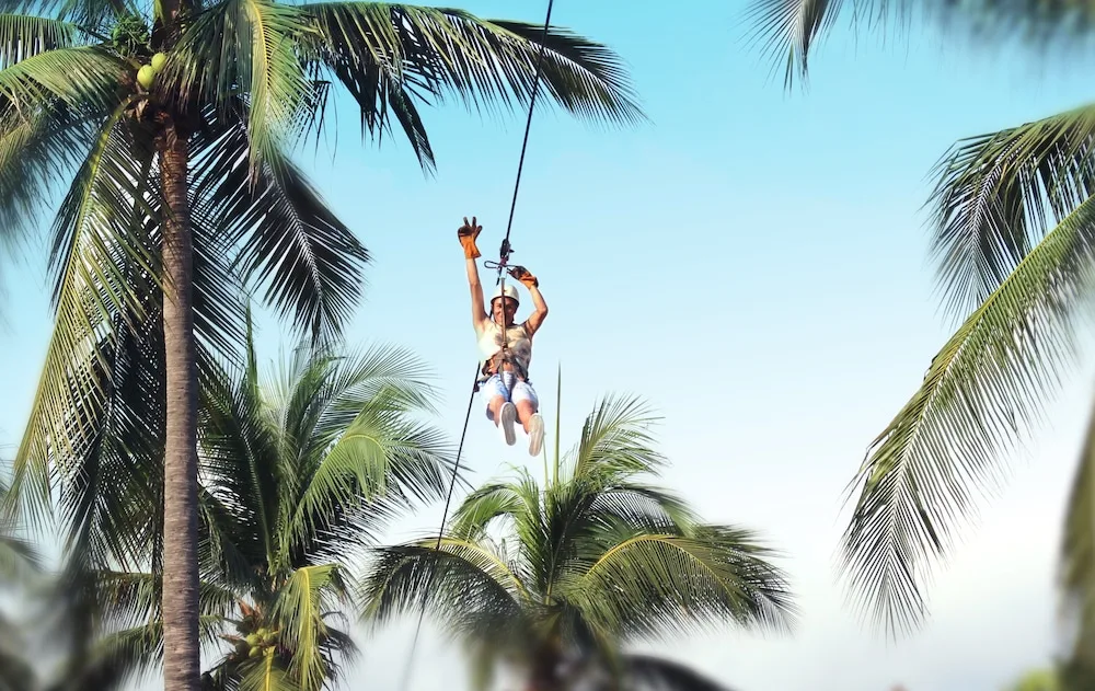 Guest riding a zip line among palm trees at Vista Playa de Oro Manzanillo.