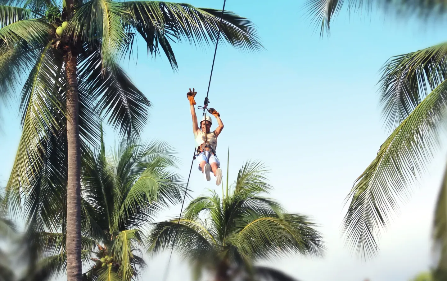Guest riding a zip line among palm trees at Vista Playa de Oro Manzanillo.