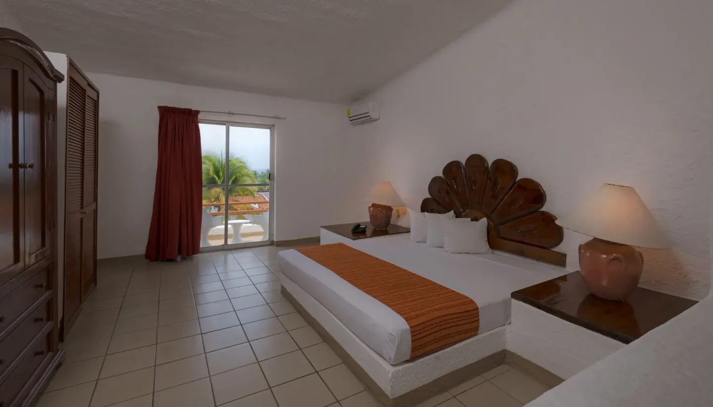 Standard Room king bed with balcony doors and wardrobe at Vista Playa de Oro Manzanillo.
