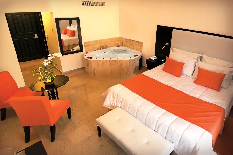 Guest room with king bed, orange accents, and corner whirlpool tub at Viva Dominicus Palace.