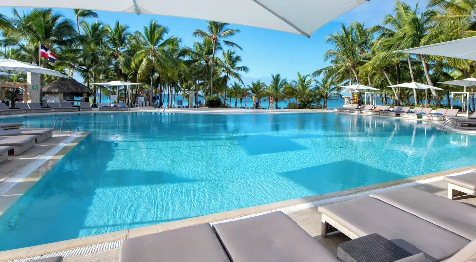 Pool with loungers, umbrellas, palms, and sea views at Viva Dominicus Palace.