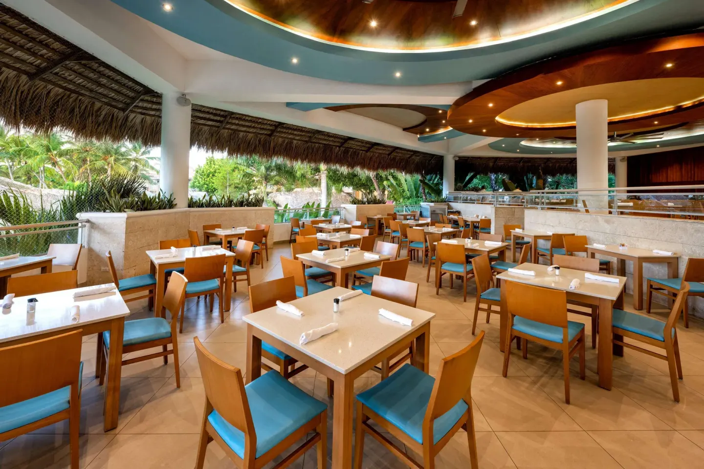 Open-air restaurant seating with teal chairs and thatched edges at Viva Dominicus Palace.