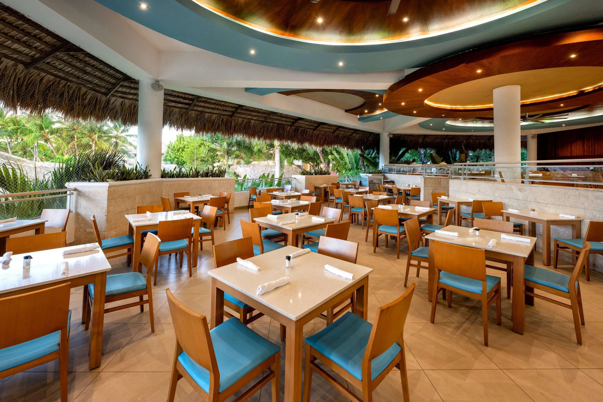 Open-air restaurant seating with teal chairs and thatched edges at Viva Dominicus Palace.