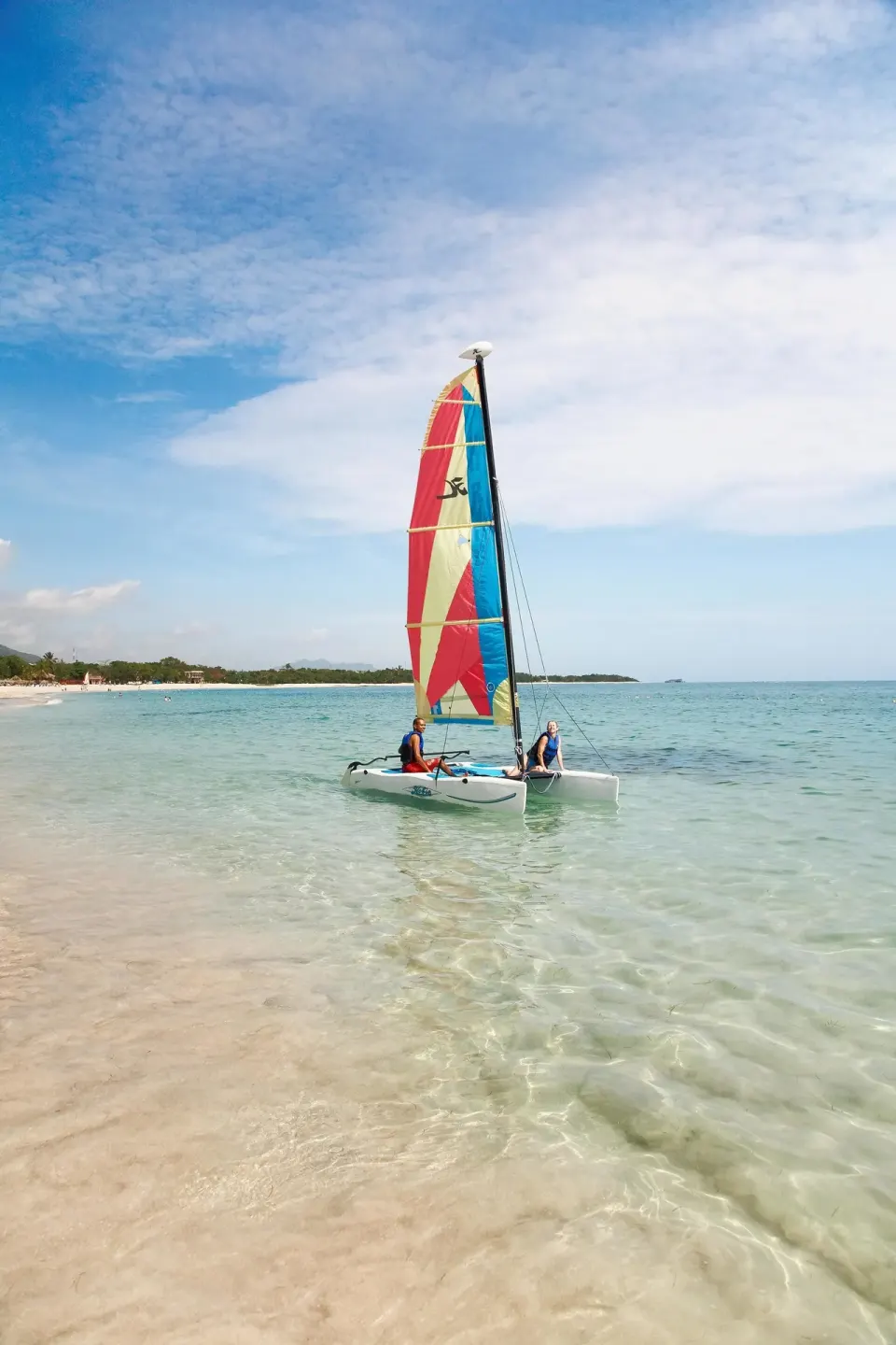 Catamaran with a colorful sail in shallow beach water at Viva Heavens.