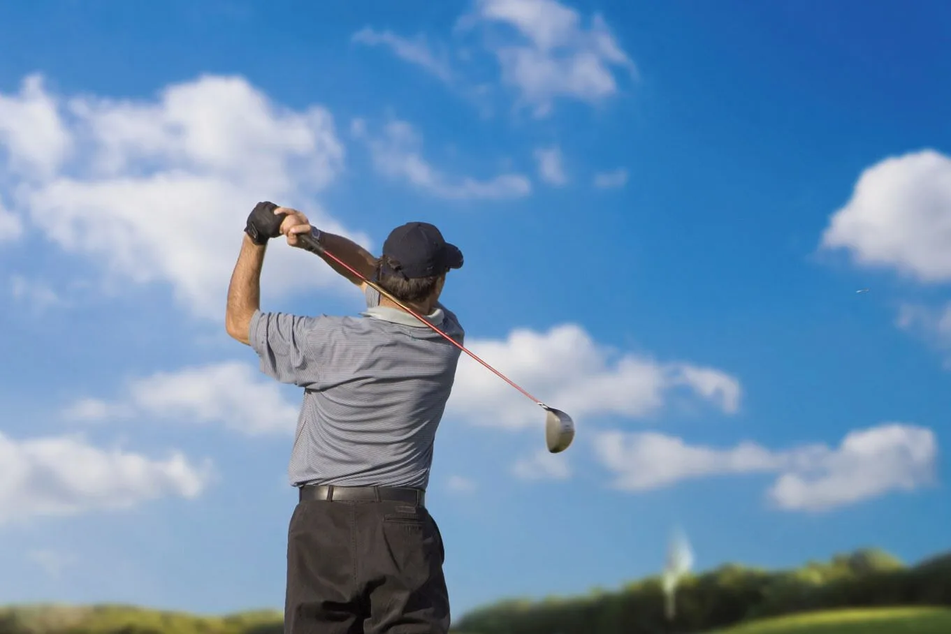 Golfer completing a swing under a blue sky at Viva Heavens.