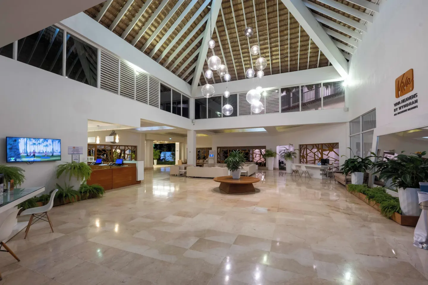 The lobby at Viva Heavens has a high pitched ceiling, reception desks, seating, and plants.