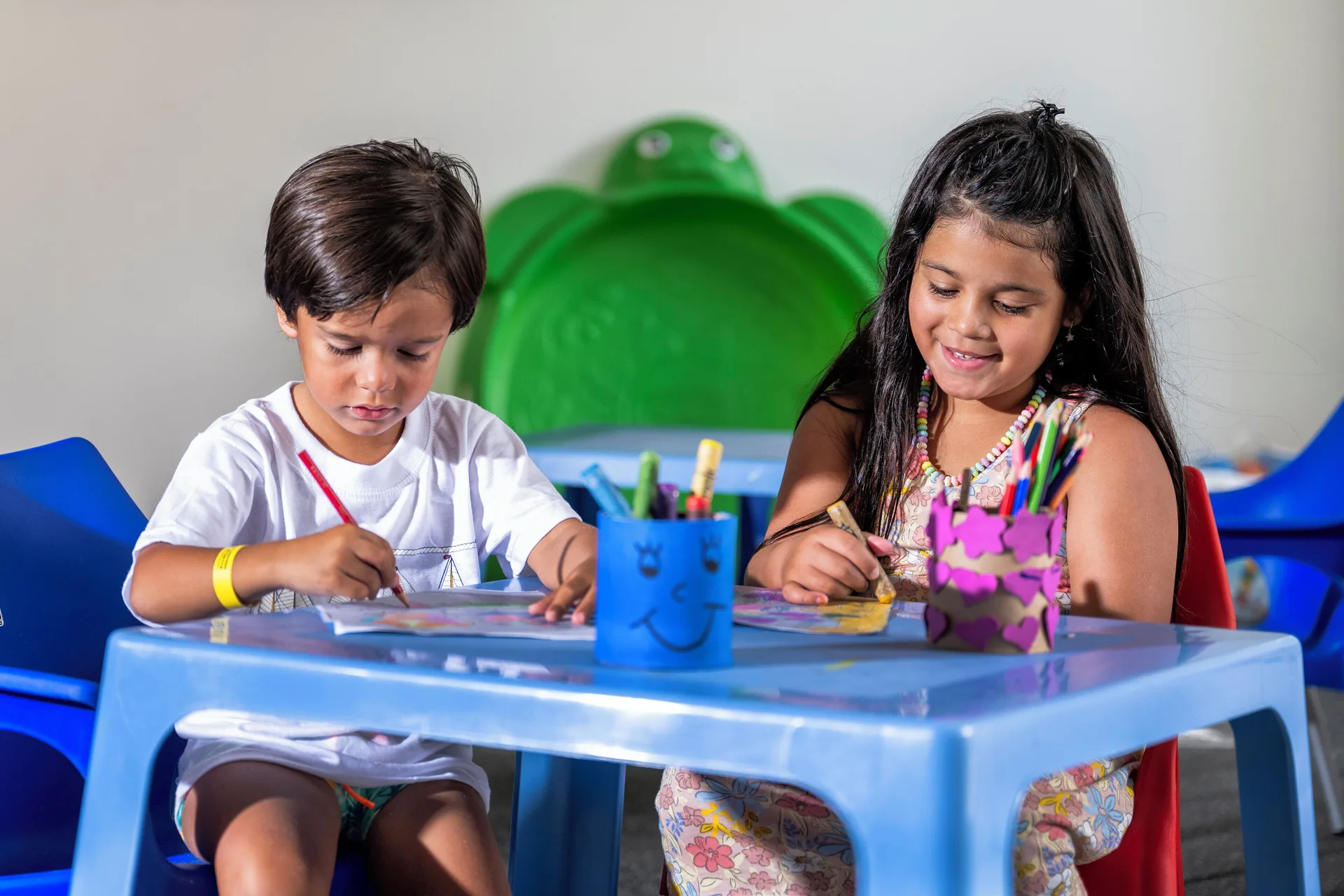 Two children coloring at a blue activity table in the kids club at Viva Heavens.