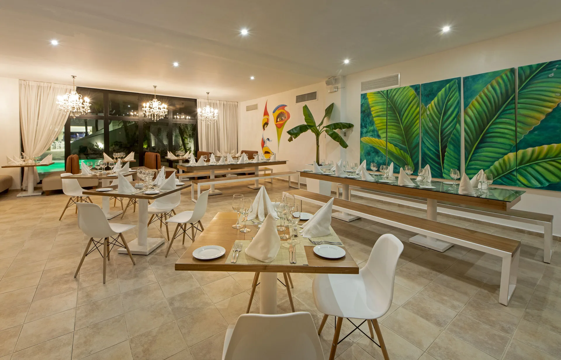 Dining room with set tables, chandeliers, and tropical leaf artwork at Viva Heavens.