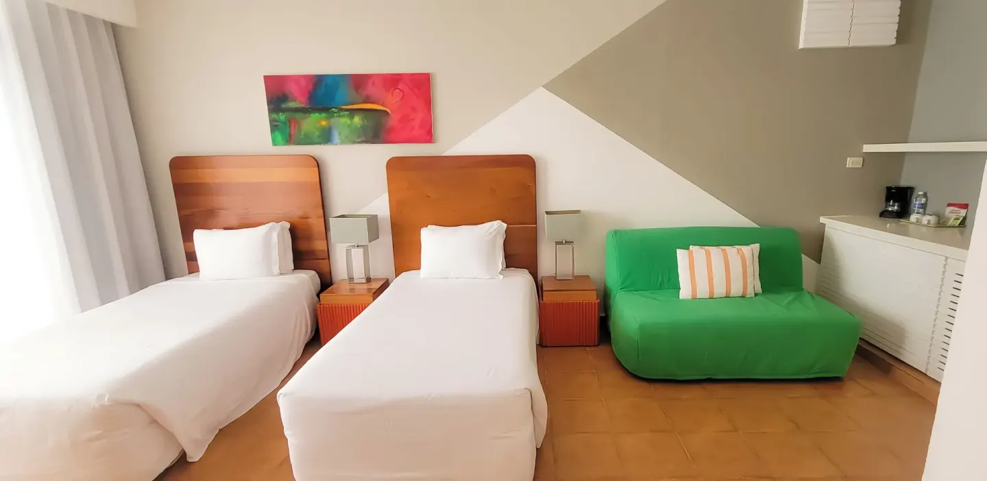 All Together Non-Smoking room with two twin beds and green sofa at Viva Heavens.