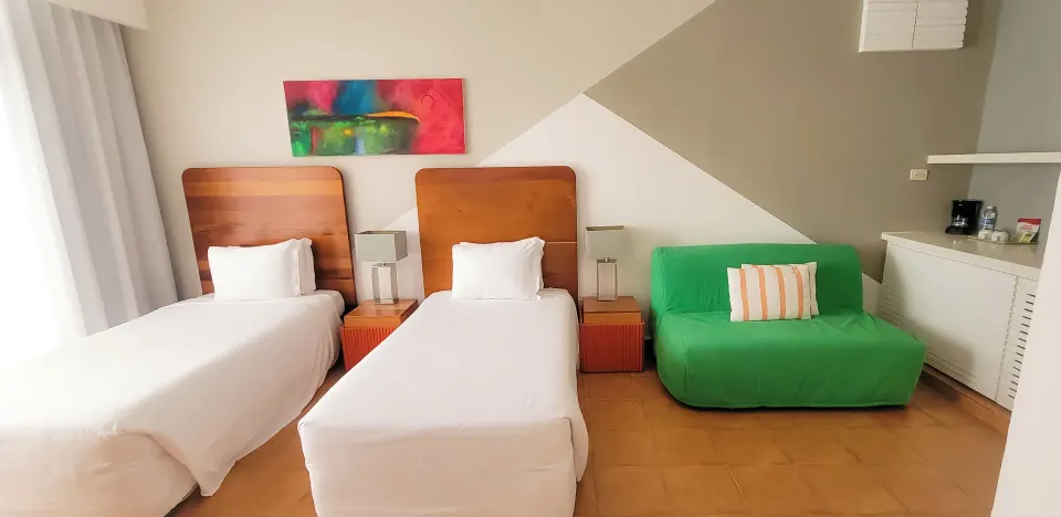 All Together Non-Smoking room with two twin beds and green sofa at Viva Heavens.