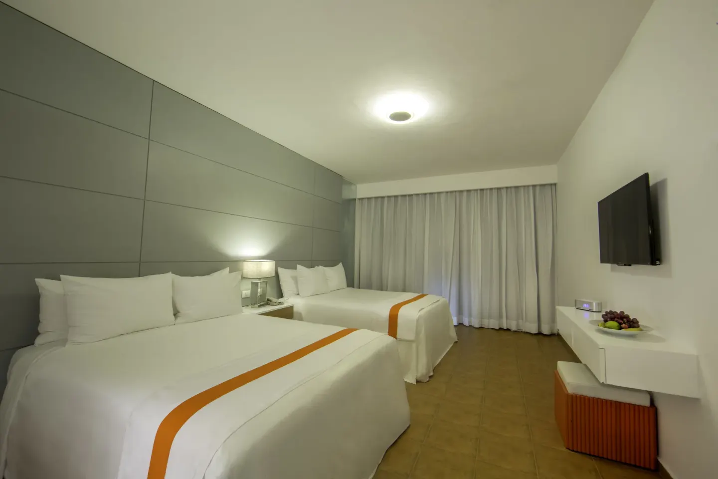 Nirvana room with two size beds, bedside lamp, TV, and white curtains at Viva Heavens.
