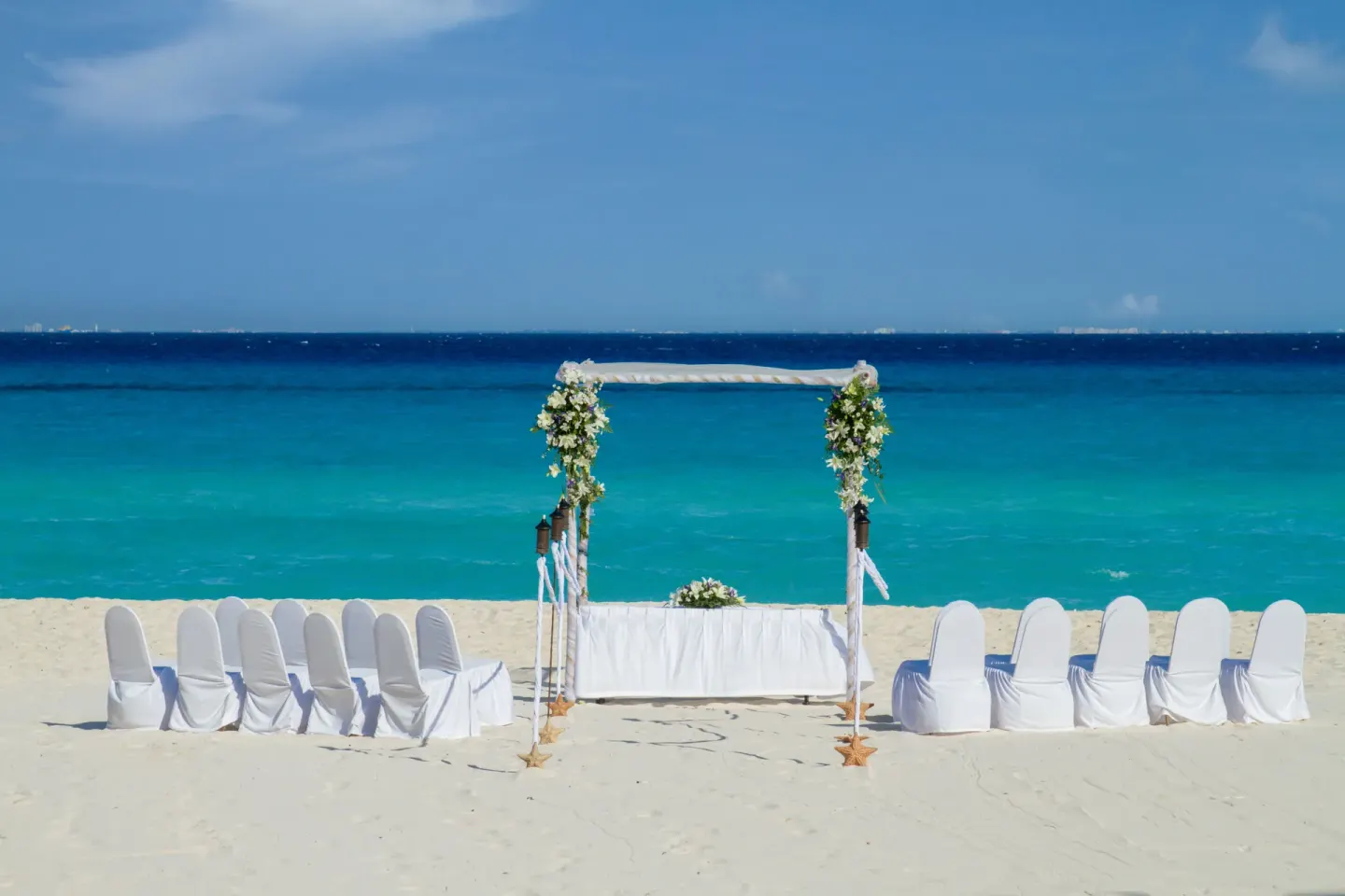 Beach wedding arch with white chairs facing turquoise water at Viva Heavens.