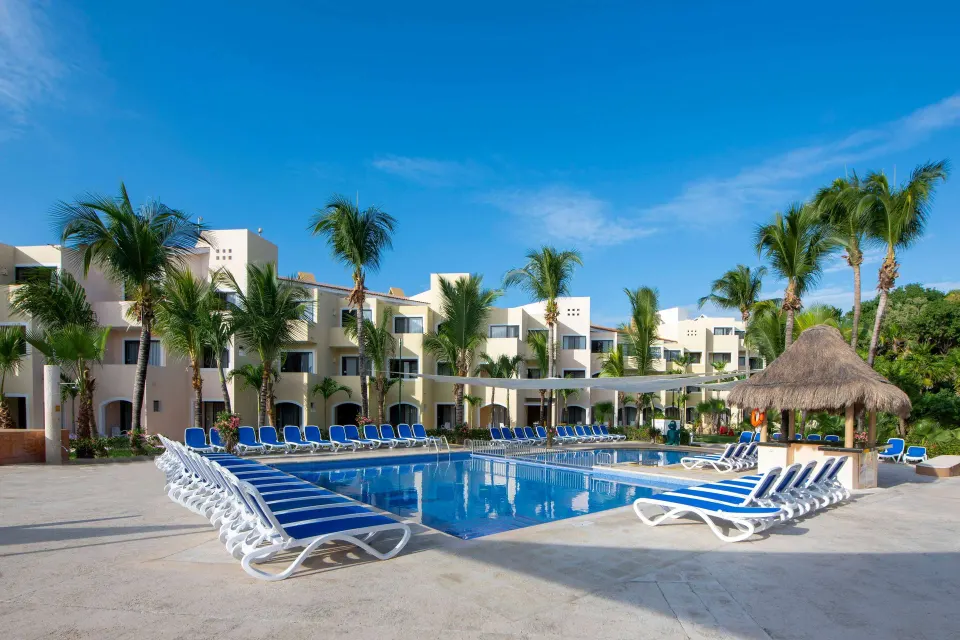 Rectangular resort pool with rows of loungers and low-rise hotel rooms at Viva Maya.