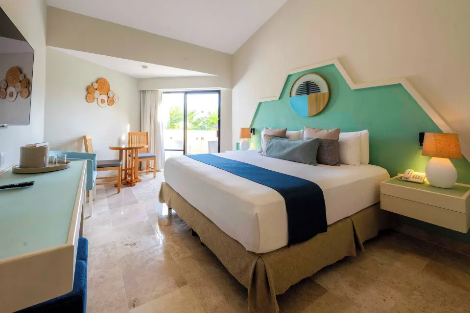 King bed and bedside lamps with patio door in a Viva Maya guest room