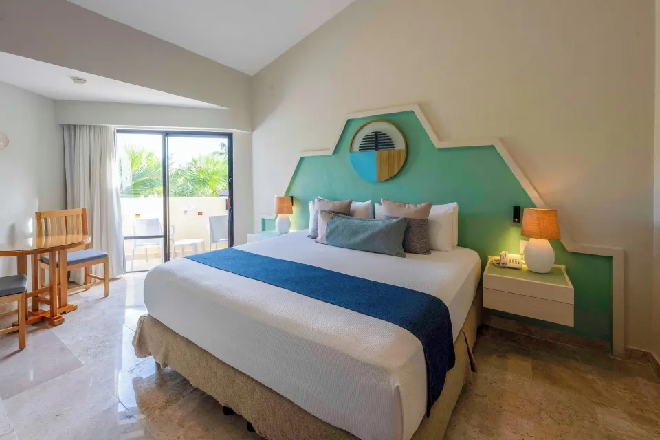 King bed and balcony in a Viva Maya guest room with turquoise headboard and seating.
