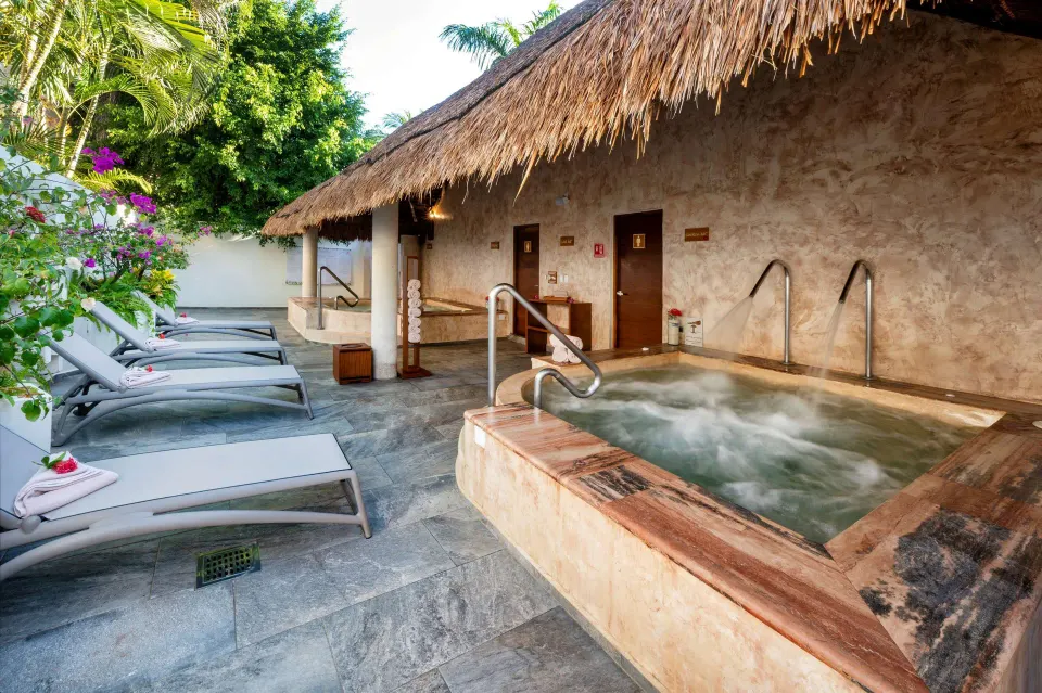 Spa relaxation area with a bubbling jacuzzi, loungers, and tropical plants at Viva Maya.
