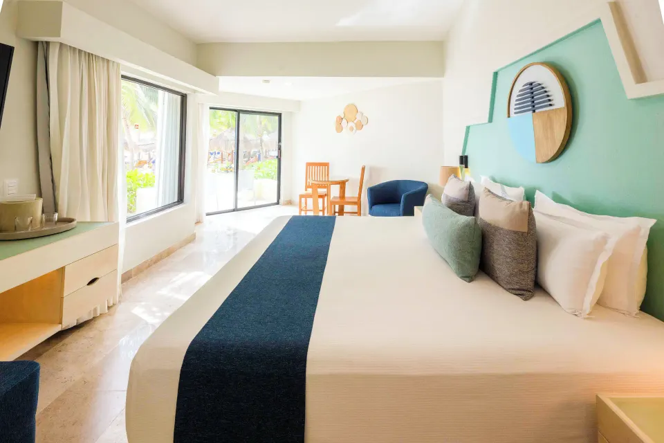 King bed with blue runner and balcony door in a Viva Maya guest room