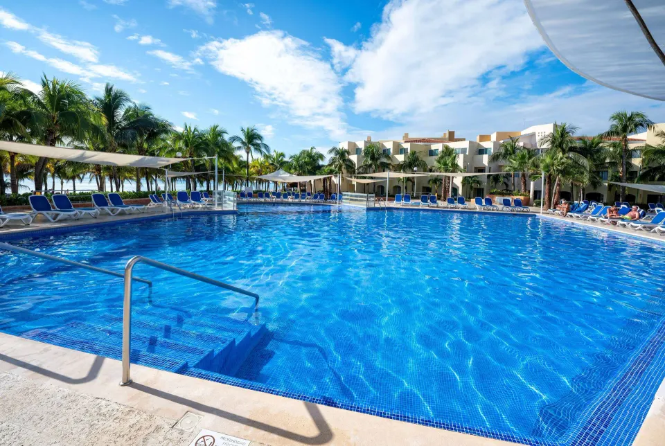Large resort swimming pool with lounge chairs and palm trees at Viva Maya.