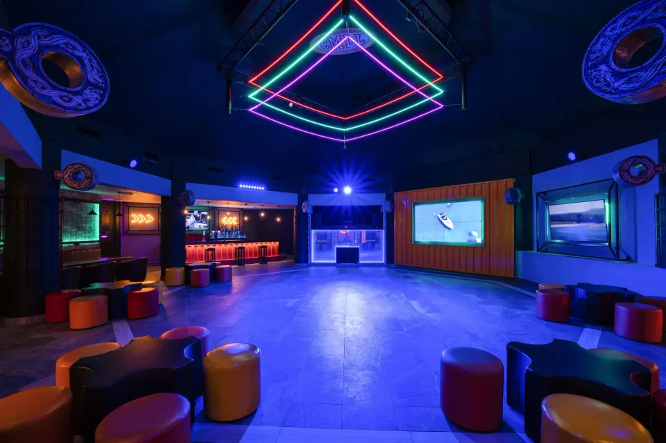 Dark nightclub room lit by colorful neon shapes and low stools at Viva Maya.