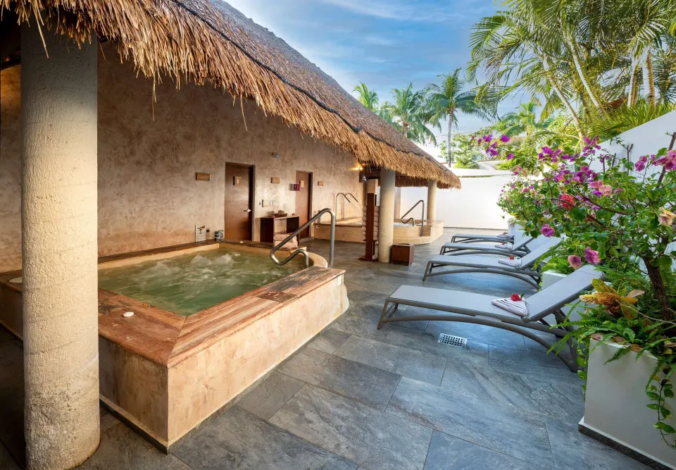 Outdoor spa area with a bubbling hot tub and lounge chairs under a palapa at Viva Maya.