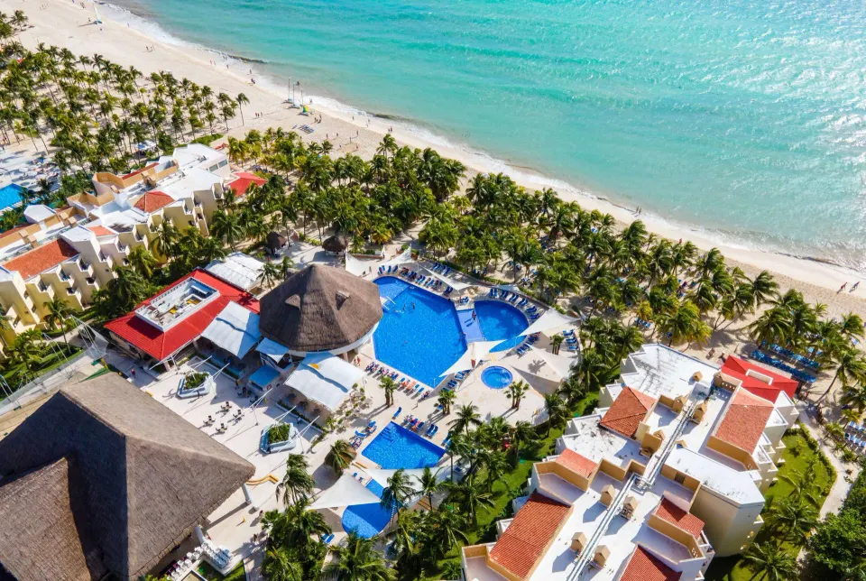 Aerial view of Viva Maya's large pool area lined with palm trees and the adjacent beach.