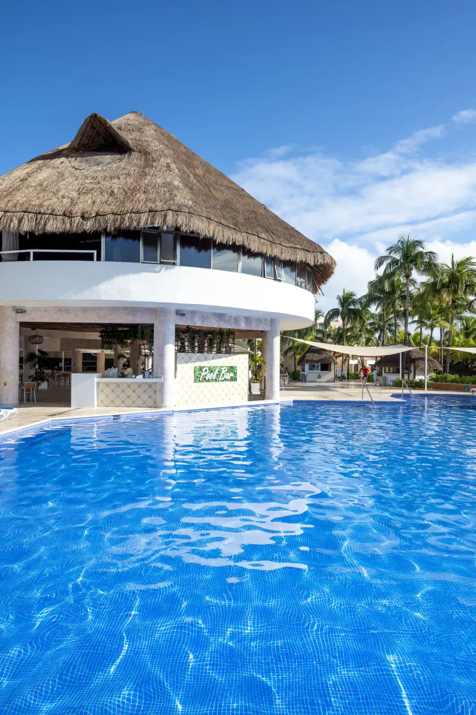 Thatched-roof pool bar and large swimming pool at Viva Maya under a blue sky.