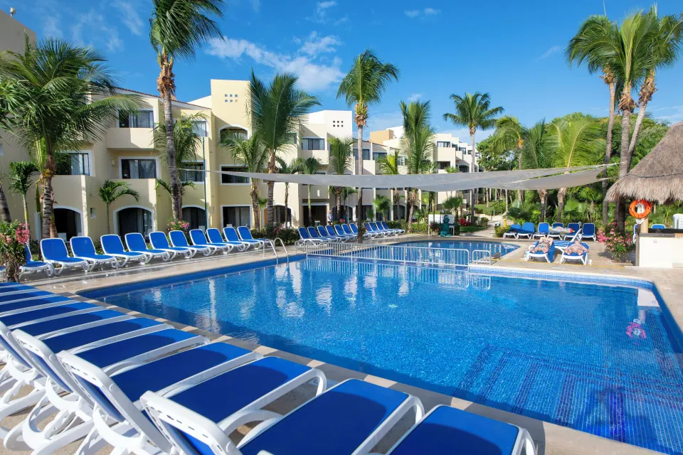 Resort swimming pool with blue loungers and palm trees at Viva Maya